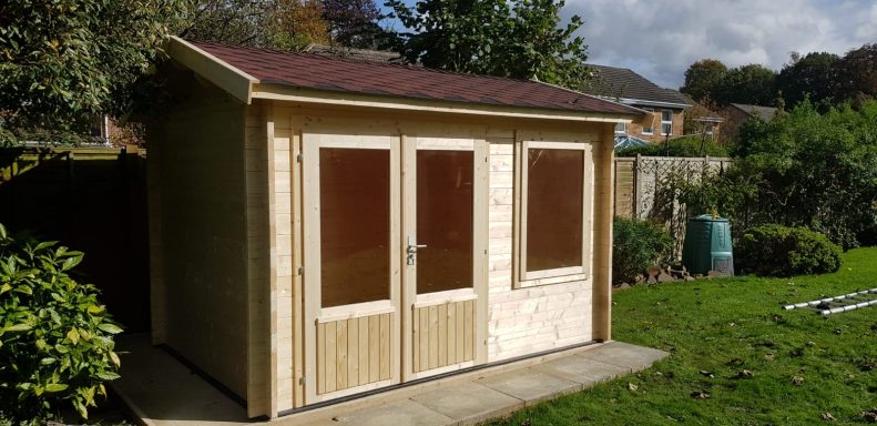 Wooden garden shed with double doors and large windows, situated in a green outdoor space.